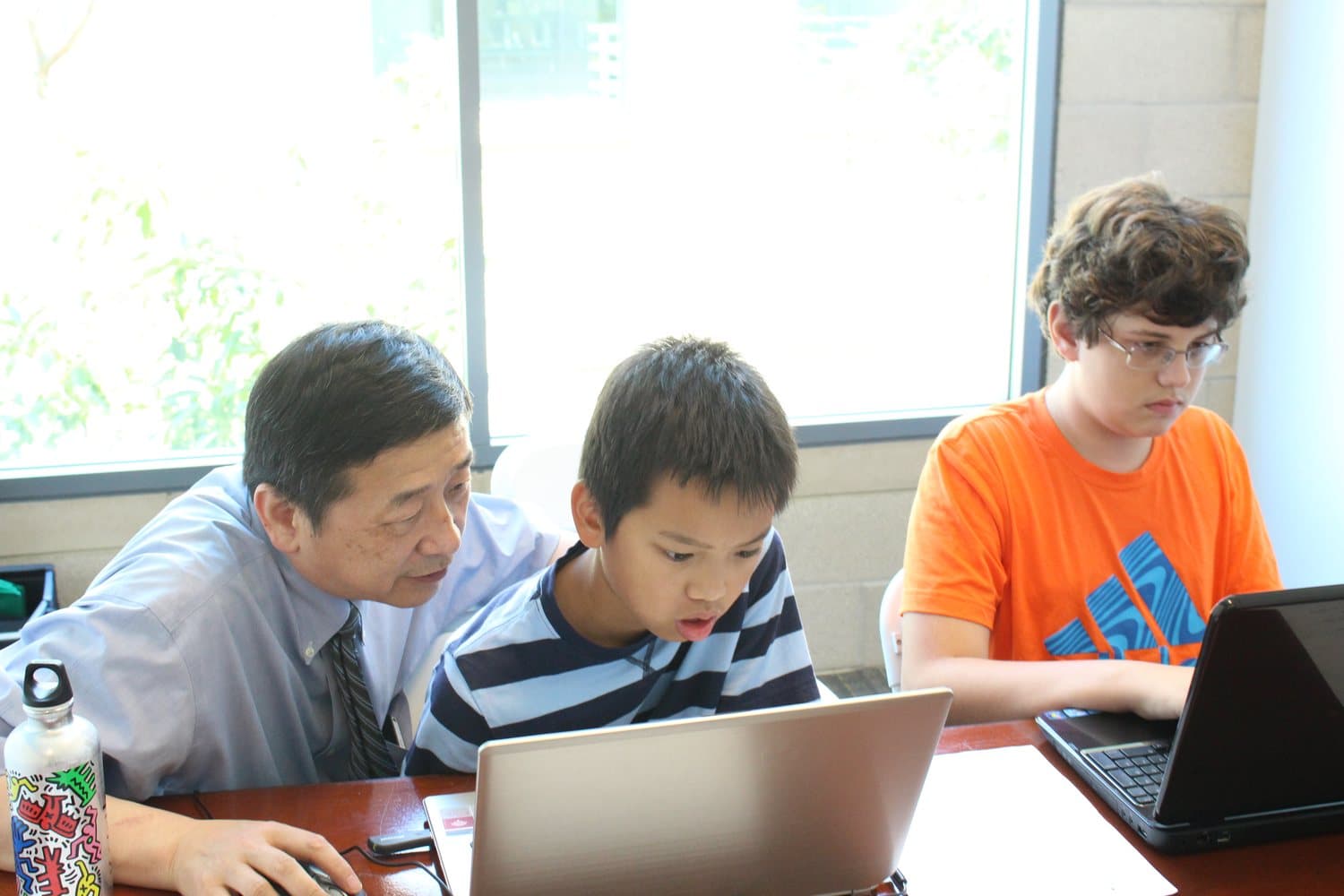 Dr. Li sitting beside a student at a laptop, reviewing code together.
