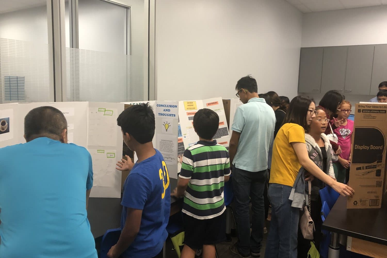 Middle-school students standing at their project boards while parents and judges listen.