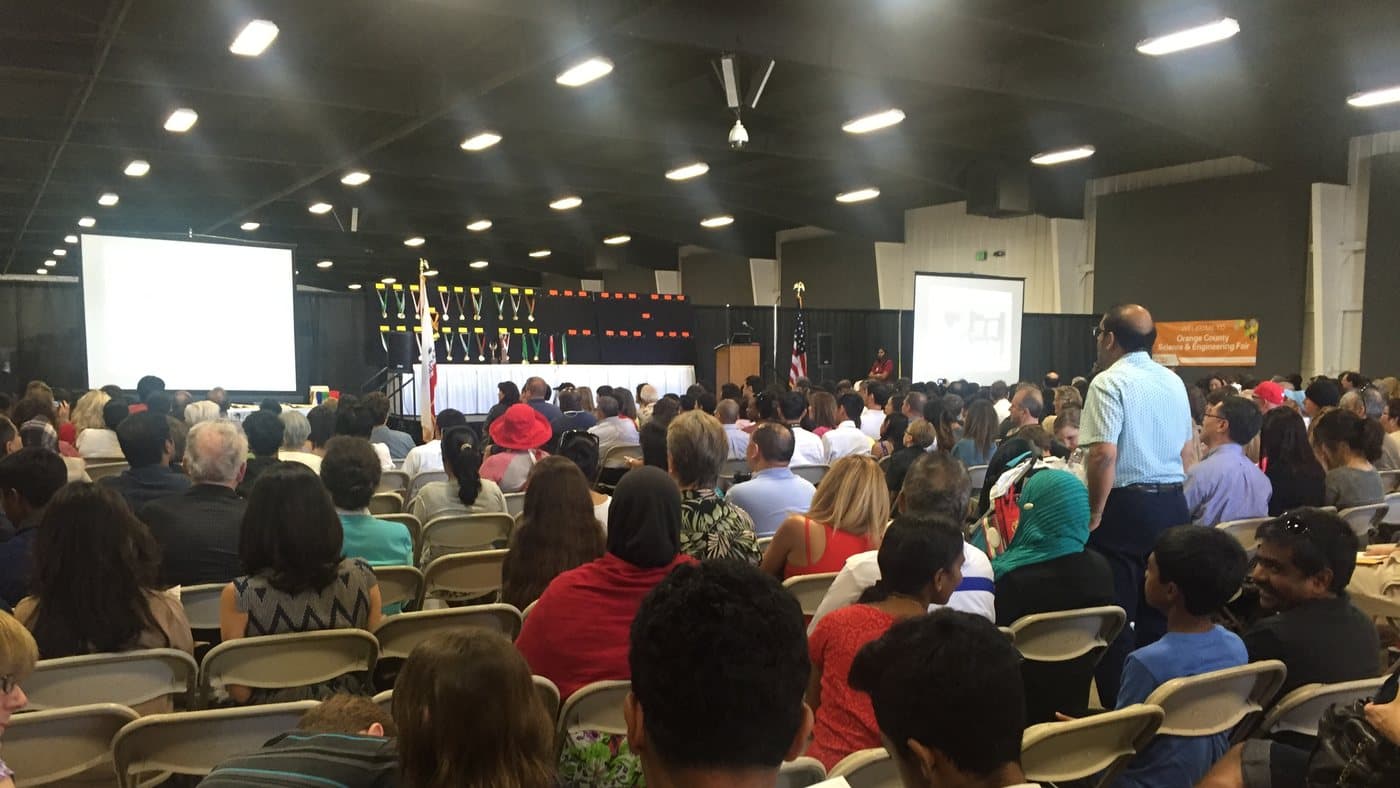 A full hall at the Orange County Science and Engineering Fair awards ceremony, trophies lined up on the stage.